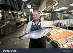 Stock Photo Male Fishmonger Wearing An Apron Holding Large And Whole Salmon Fish In Front Of Display Counter 742431265